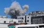 Displaced Palestinians sitting in the back of a truck laden with their belongings while fleeing bombardment, watch smoke billowing amid Israeli strikes on Al-Shati camp for Palestinian refugees west of Gaza City on September 18, 2025. (Photo by Omar Al-Qattaa / AFP)
