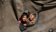 Children look on from a hole behind the canvas of a tent at a camp for people displaced by war in northern Nuseirat in the central Gaza Strip on October 7, 2025. (Photo by Bashar Taleb / AFP)