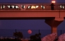 The full moon rises on the horizon as a metro train passes in Doha on October 7, 2025. (Photo by Karim Jaafar / AFP)