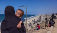 A Palestinian woman holding a child watches people walking along Al-Rashid road toward Gaza City from Nuseirat in the central Gaza Strip on October 10, 2025. (Photo by Bashar Taleb / AFP)