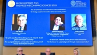 (L-R) John Hassler, Chair of the Committee for the Prize in Economic Science in Memory of Alfred Nobel, the Secretary General of the Royal Swedish Academy of Sciences Hans Ellegren and Kerstin Enflo, member of the Committee for the Prize in Economic Sciences in Memory of Alfred Nobel sit in front of a screen displaying the portraits of the 2025 prize winners. (Photo by Anders Wiklund / TT NEWS AGENCY / AFP) 