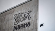 This photograph shows a bird flying next to the logo of Swiss food giant Nestle on the facade of its headquarters, in Vevey, western Switzerland, on October 14, 2025. (Photo by Fabrice Coffrini / AFP)