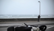 A person holds on to a lamppost as an overturned scooter is seen on a street on October 23, 2025 in San Sebastian, northern Spain, amid strong winds and a rough sea. (Photo by ANDER GILLENEA / AFP)
