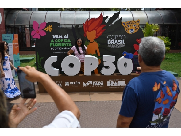 A tourist poses for a picture with COP30 mascot inside the Estacao das Docas, a tourist port area in Belem, Para State, Brazil on November 7, 2025. The COP30 UN Climate Change Conference takes place from November 10 to 21, in Belem, Para state, Brazil. (Photo by MAURO PIMENTEL / AFP)
