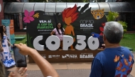 A tourist poses for a picture with COP30 mascot inside the Estacao das Docas, a tourist port area in Belem, Para State, Brazil on November 7, 2025. The COP30 UN Climate Change Conference takes place from November 10 to 21, in Belem, Para state, Brazil. (Photo by MAURO PIMENTEL / AFP)
