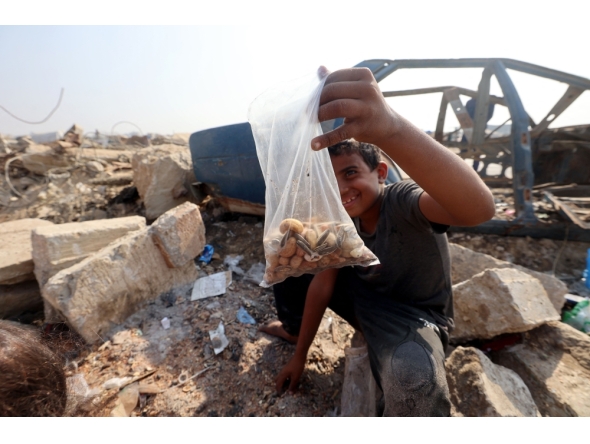 A Palestinian boy shows a bag of seeds and nuts he collected from the sand along the verge of a road near in the Nuseirat refugee camp in the central Gaza Strip, on November 9, 2025. (Photo by Eyad Baba / AFP)