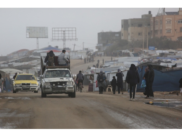 Displaced Palestinian walk past a vehicle carrying others west of Deir al-Balah city in the central Gaza Strip, on November 15, 2025 as a low-pressure system impacts the area. (Photo by Bashar TALEB / AFP)