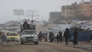 Displaced Palestinian walk past a vehicle carrying others west of Deir al-Balah city in the central Gaza Strip, on November 15, 2025 as a low-pressure system impacts the area. (Photo by Bashar TALEB / AFP)