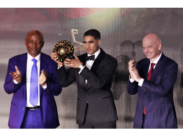 Paris Saint-Germain's Moroccan defender Achraf Hakimi (C) holds his Africa Player of the Year award next to CAF President Patrice Motsepe (L) and FIFA President Gianni Infantino (R) during the 2025 Confederation of African Football (CAF) Awards in Sale, Morocco on November 19, 2025. Photo by Abdel Majid Bziouat / AFP