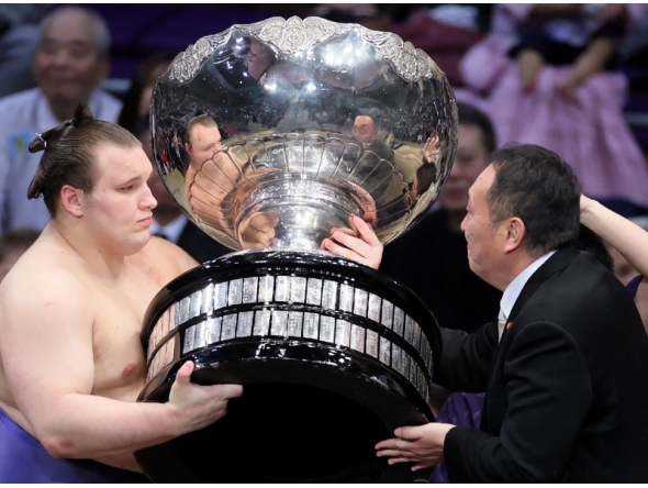 Ukrainian sumo wrestler Danylo Yavhusishyn, also known by his Japanese ring name Aonishiki Arata (L), receives the Prime Minister's Cup trophy after winning the Grand Sumo Tournament in Fukuoka on November 23, 2025. (Photo by JIJI PRESS / AFP) 