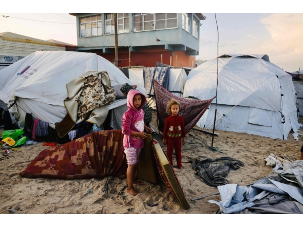 Palestinian children move mattresses to protect them from the rain at a makeshift camp housing displaced Palestinians in Deir al-Balah on November 25, 2025. (Photo by Bashar Taleb / AFP)