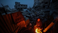 A displaced Palestinian woman warms herself beside a fire amid the ruins of destroyed buildings in the Bureij refugee camp, in the central Gaza Strip, on November 29, 2025. (Photo by Eyad Baba / AFP)
