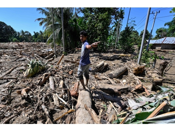 A man walks across mud and debris in a flood affected area in Meureudu, Pidie Jaya district in Indonesia's Aceh province on November 30, 2025. (Photo by Chaideer Mahyuddin / AFP)
