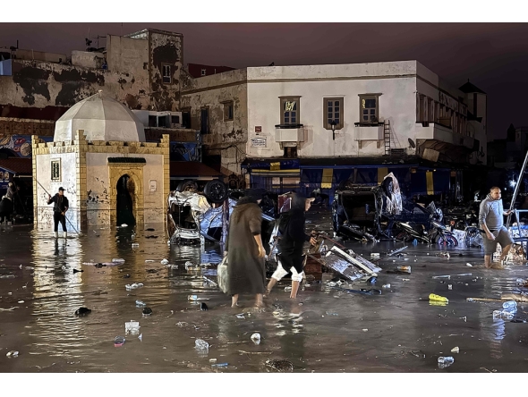 People wade through a square after a flash flood in Safi on December 14, 2025. Flash-flooding caused by sudden, heavy rain killed at least 21 people in the Moroccan coastal town of Safi on December 14, local authorities said. (Photo by AFP)