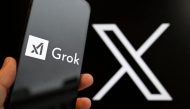 (Files) This photograph shows a smartphone bearing the logo of Grok in front of the X logo in Brussels on January 12, 2026. (Photo by Nicolas Tucat / AFP)