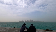 Visitors sit along the waterfront on a foggy day at the Corniche area facing the high-rise buildings in the West Bay district, in Doha on January 15, 2026. (Photo by Karim JAAFAR / AFP)
