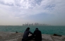 Visitors sit along the waterfront on a foggy day at the Corniche area facing the high-rise buildings in the West Bay district, in Doha on January 15, 2026. (Photo by Karim JAAFAR / AFP)
