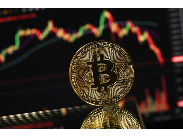 (Files) An illustration photograph taken on November 22, 2025, shows a gold plated souvenir Bitcoin coin reflected in a mirror and arranged for a photograph in front of a computer screen displaying the Bitcoin monthly price chart in a residential property in Guildford, south of London. (Photo by Justin Tallis / AFP)