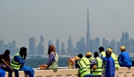 (Files) Workers sit on a wall against the backdrop of the Dubai city skyline on March 11, 2026. (Photo by Giuseppe Cacace / AFP)