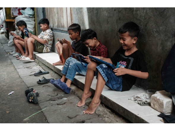 Children play online games against each other on smartphones and tablets along an alley in Jakarta on March 26, 2026. Photo by YASUYOSHI CHIBA / AFP