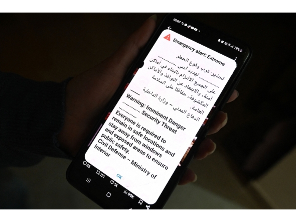 A Kuwaiti woman holds her phone displaying an alert message as sirens sound during an Iranian missile or drone attack in Kuwait City early on March 31, 2026. (Photo by Yasser Al-Zayyat/ AFP)