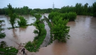 A man walks along a flooded path as torrential rains cause water channels to overflow, inundating nearby areas of Peshawar on April 7, 2026. Photo by Abdul MAJEED / AFP