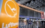 The logo of German airline Lufthansa is seen in the foreground as passengers walk below a flight information display at Frankfurt Airport, Frankfurt am Main, western Germany, on April 15, 2026, as cabin crew union UFO urged members of Lufthansa cabin crew to stage a strike in a dispute over pay and pensions. Photo by Kirill KUDRYAVTSEV / AFP