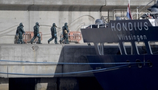 Persons wearing protective suits walk toward the hantavirus-stricken cruise ship MV Hondius docked in the port of Granadilla de Abona on the island of Tenerife in Spain's Canary Islands on May 11, 2026. (Photo by JORGE GUERRERO / AFP)