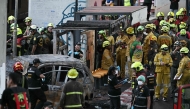 Forensic police officers, rescue workers and firefighters stand at the site of a train collision with a bus underneath Makkasan Airport Rail station in Bangkok on May 16, 2026. (Photo by Lillian SUWANRUMPHA / AFP)