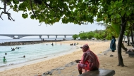 A man sits under a tree as it rains at Artificial Beach in Malé on May 15, 2026. Photo by MOHAMED AFRAH / AFP