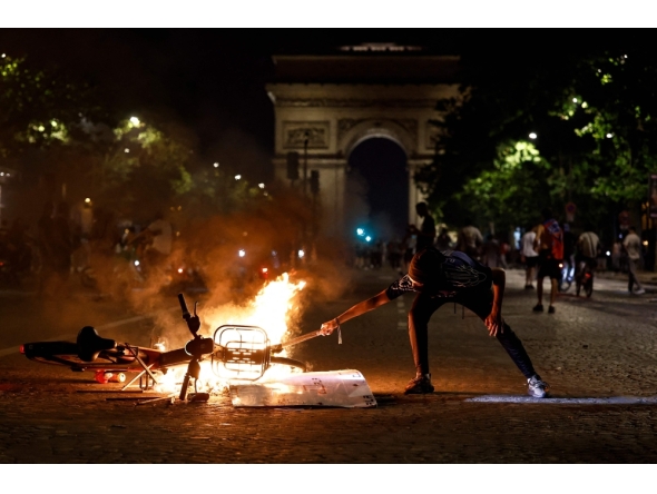 A member of the public holds an object to a burning bicycle on the Avenue de la Grande Armee during gatherings after PSG won the UEFA Champions League final between Paris Saint-Germain (PSG) and Arsenal FC played in Budapest (Photo by Kenzo Tribouillard / AFP)