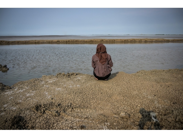A resident affected by the Lapindo mudflow sits on the embankment in the mud volcano area, marking 20 years since a gas exploration accident triggered a mud flow that inundated more than a dozen villages and permanently displaced tens of thousands of people in Porong, Sidoarjo, East Java province on May 29, 2026. (Photo by JUNI KRISWANTO / AFP)