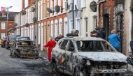 Residents and members of the media look at burnt-out cars and homes after demonstrations turned violent the night before, in eastern Belfast, Northern Ireland, on June 10, 2026. Photo by Paul Faith / AFP