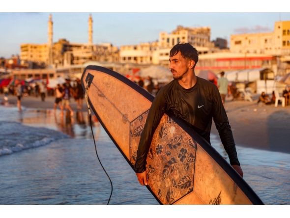 Palestinian surfer Tahseen Abu Assi, 23, takes his surfboard out into the Mediterranean sea off a beach in Gaza City on June 21, 2026. (Photo by Omar Al-Qattaa / AFP)