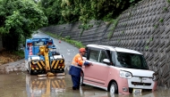 A tow lorry driver retrieves a partially submerged car after flooding in the town of Kashiwara, Osaka prefecture on June 26, 2026.  (Photo by Paul Miller/ AFP)