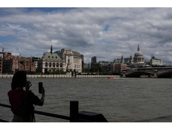 A woman takes a photo toward St. Paul's from the south side of the River Thames in central London on June 28, 2026, as people come out to take advantage of cooler temperatures following days of extreme heat. The UK broke the record for a June temperature for the third day in a row on June 26, the Met Office weather agency said, as a sweltering heatwave strained schools and hospitals and drove down business. (Photo by CARLOS JASSO / AFP)