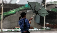 A woman struggles with an umbrella in strong winds and rain as typhoon Bavi passes off northeastern Taiwan in Keelung on July 11, 2026. More than 14,000 people in Taiwan have fled their homes, and many shops remain closed, as a typhoon pounding Japan's remote southwestern islands swept towards China on July 11. (Photo by I-Hwa Cheng / AFP)