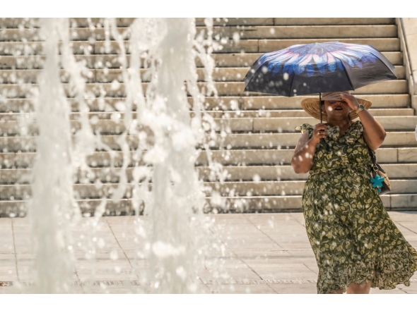 A woman protects herself from the sun with an umbrella as she walks through Athens' main square of Syntagman on July 21, 2026. (Photo by Aris Messinis / AFP)
 