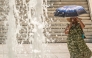 A woman protects herself from the sun with an umbrella as she walks through Athens' main square of Syntagman on July 21, 2026. (Photo by Aris Messinis / AFP)
 