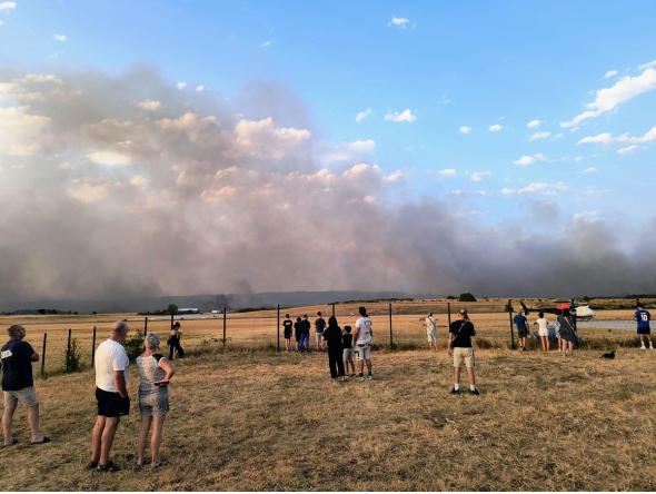 Bystanders look on as fire and smoke billow across Castres-Mazamet aerodrome, near Labruguiere in south-western France on July 24, 2026. (Photo by Daniel ABELOUS / AFP)

