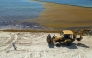 This aerial view shows a backhoe loader removing accumulated sargassum seaweed from the shoreline as a municipal worker walks along a beach in Playa del Carmen, Quintana Roo State, Mexico, on August 6, 2026. (Photo by Alfredo ESTRELLA / AFP)