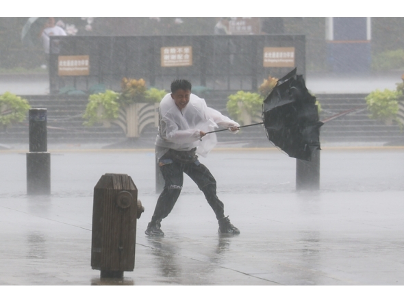 A man holds tightly onto an umbrella that is blown open by the wind amid rain at Huangpu District of Shanghai, east China, on Aug. 9, 2026. (Xinhua/Wang Xiang)