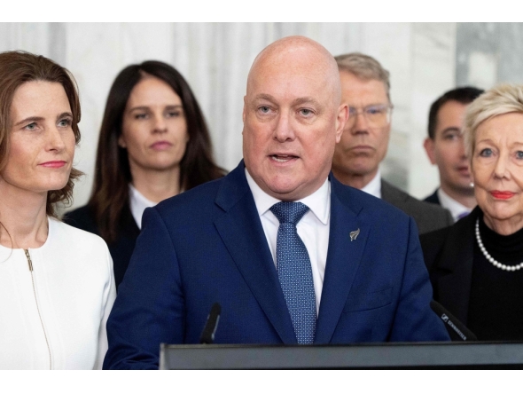 New Zealand Prime Minister Chris luxon, flanked my his caucus, speaks to the media after surviving a 2nd National party leadership vote at Parliament in Wellington on August 12, 2026. (Photo by Marty MELVILLE / AFP)