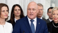 New Zealand Prime Minister Chris luxon, flanked my his caucus, speaks to the media after surviving a 2nd National party leadership vote at Parliament in Wellington on August 12, 2026. (Photo by Marty MELVILLE / AFP)