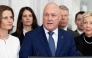 New Zealand Prime Minister Chris luxon, flanked my his caucus, speaks to the media after surviving a 2nd National party leadership vote at Parliament in Wellington on August 12, 2026. (Photo by Marty MELVILLE / AFP)