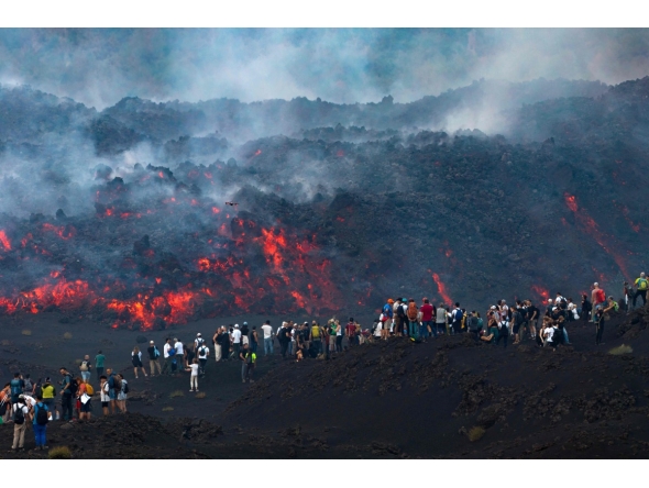This handout photograph taken by Etna Walk on August 11, 2026 and obtained on August 12, 2026 shows visitors standing next to lava flowing from Mount Etna volcano during an eruption, in Catania, in the Mediterranean island of Sicily. (Photo by Handout / Etna Walk / AFP)
