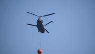 A Royal Netherlands Air Force Boeing CH-47D Chinook carrying a bambi bucket departs from Baelen, near Eupen, eastern Belgium to tackle a wildfire burning in the Hautes Fagnes (High Fens) nature reserve on August 16, 2026. Photo by JOHN THYS / AFP