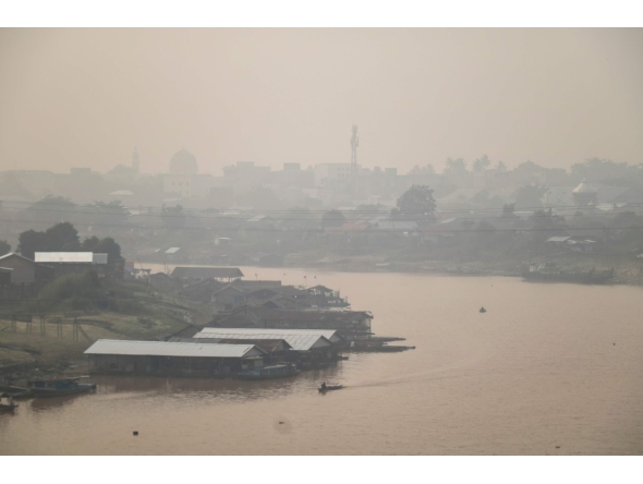Haze blankets a riverside residential area along the Kahayan River in Palangkaraya, Central Kalimantan, on August 21, 2026, as a result of widespread forest and land fires occurring at various points across the island. (Photo by REINA / AFP)