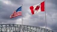 The US and Canadian flags flutter next to the Blue Water Bridge border crossing in Point Edward, Ontario, on October 24, 2025. (Photo by Geoff Robins / AFP)