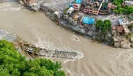 An aerial view shows a collapsed bridge along with houses lying deluged in sludge after flash floods at Devighat, Bidur Municipality in nepal's Nuwakot district on August 27, 2026.  (Photo by Prabin RANABHAT / AFP)